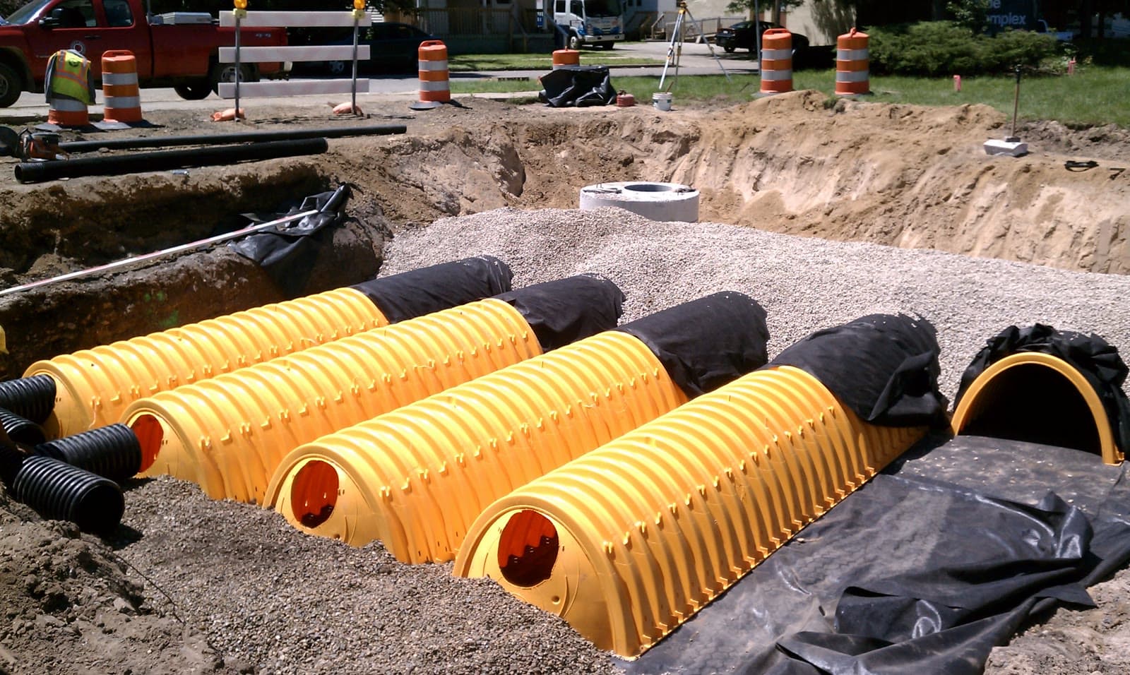 Yellow arched underground stormwater detention chambers under construction in a parking lot.